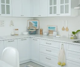 White corner kitchen with glass-front upper cabinets, panelled drawers and a light benchtop